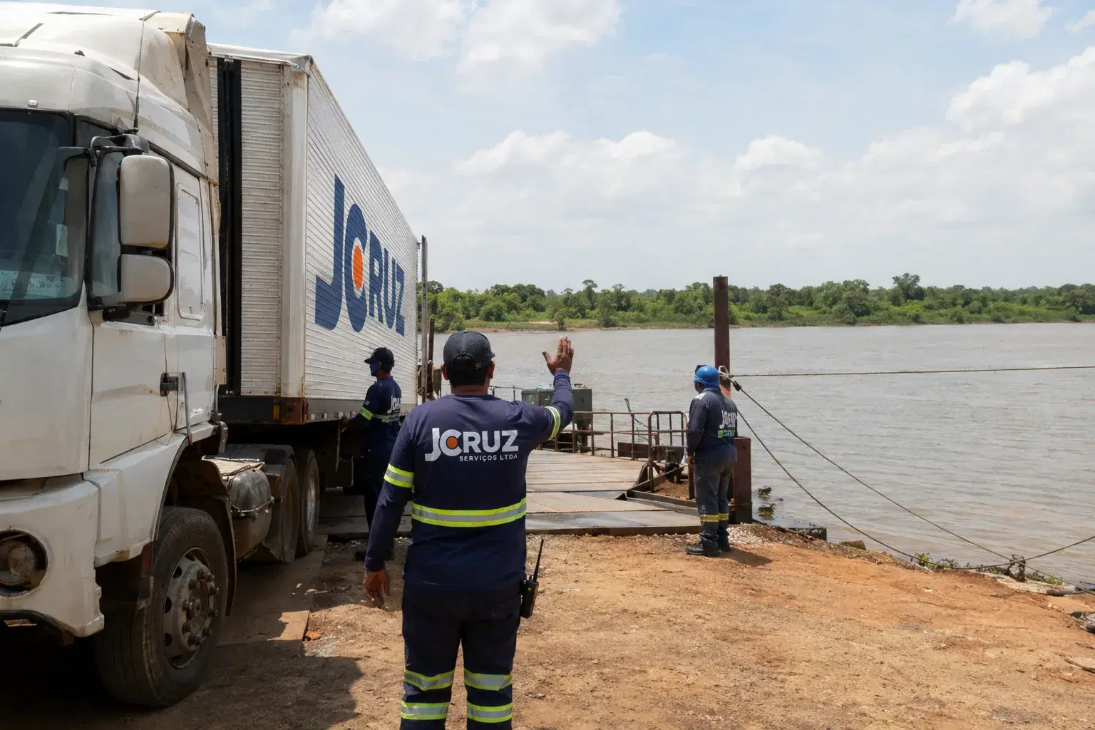 Equipe da J Cruz orientando o embarque de um caminhão em balsa na margem do rio